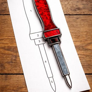 May include: A detailed image of a craft knife with a vibrant red handle and a silver blade. The knife is placed on a white paper with a numbered diagram of the knife. The background is a wooden surface.