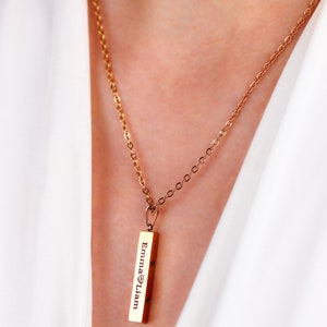 Op de afbeelding: Een gouden ketting met een staafhanger gegraveerd met de namen "Emma" en "Liam", gescheiden door een hartje.