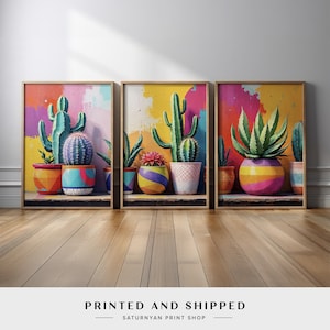 May include: Three framed art prints featuring colorful cactus plants in decorative pots. The artwork has a vibrant, abstract background with splashes of yellow, pink, and blue. The text "PRINTED AND SHIPPED" is at the bottom.