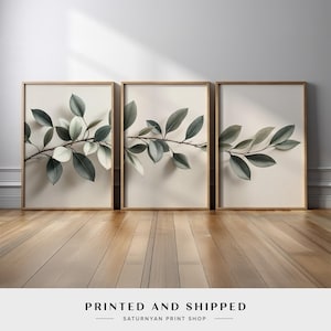 May include: Three framed botanical prints featuring watercolor-style branches with green and white leaves. The prints are in light brown wooden frames, set against a cream-colored background. The text "PRINTED AND SHIPPED" is at the bottom.