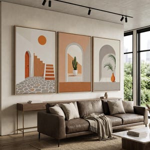 May include: A triptych of framed wall art prints featuring architectural scenes. The left print shows a stone courtyard with stairs and an orange door. The middle print depicts a cactus in an archway. The right print shows a palm in a vase.