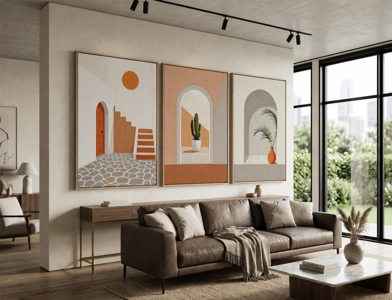 May include: A triptych of framed wall art prints featuring architectural scenes. The left print shows a stone courtyard with stairs and an orange door. The middle print depicts a cactus in an archway. The right print shows a palm in a vase.