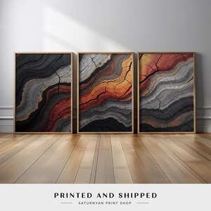 May include: Three abstract art prints with a wood grain texture and a swirling pattern of black, gray, orange, and gold colors. The prints are framed in a light wood frame.