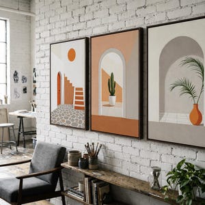 May include: A set of three framed wall art prints featuring architectural scenes. The first shows a staircase and orange sun, the second a potted cactus in an archway, and the third a palm plant in a vase within a neutral-toned arched alcove.