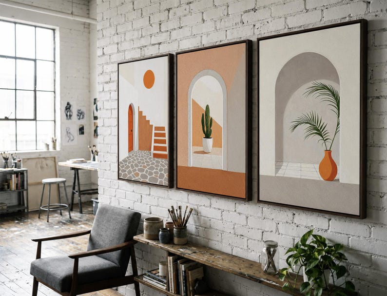 May include: A set of three framed wall art prints featuring architectural scenes. The first shows a staircase and orange sun, the second a potted cactus in an archway, and the third a palm plant in a vase within a neutral-toned arched alcove.