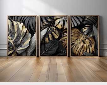 May include: Three framed art prints featuring stylized monstera leaves in shades of black, gold, and gray. The botanical prints have a modern aesthetic and are displayed on a wooden floor. The text "PRINTED AND SHIPPED" is visible at the bottom.