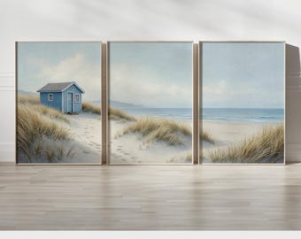 May include: Set of three framed art prints depicting a serene beach scene. The prints feature a blue beach hut, sand dunes with tall grass, and a view of the ocean under a cloudy sky. The text "PRINTED AND SHIPPED" is at the bottom.