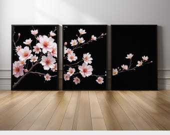 May include: Set of three framed art prints featuring watercolor cherry blossom branches with pink flowers against a black background. The prints are displayed on a wooden floor. The text "PRINTED AND SHIPPED" is at the bottom.