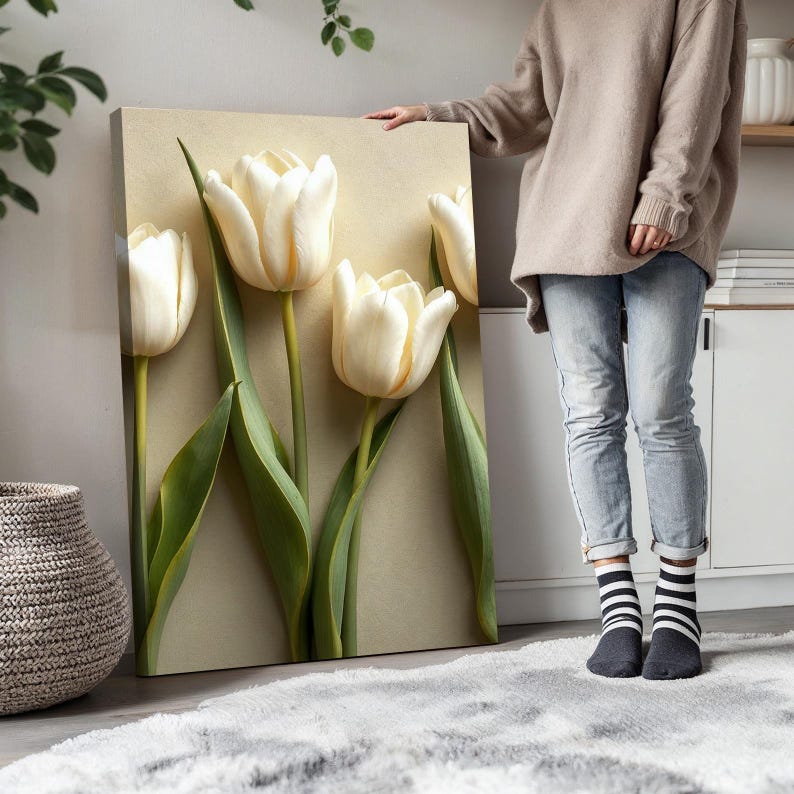 May include: A canvas art print featuring four large, creamy white tulips with green stems and leaves against a neutral background. The tulips are in full bloom, creating a sense of depth and texture. The artwork is displayed indoors.