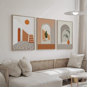 May include: A set of three framed wall art prints featuring architectural scenes. The first shows a stone patio, orange door, and stairs. The second depicts an arched doorway with a potted cactus. The third displays an arched entryway with a palm plant.