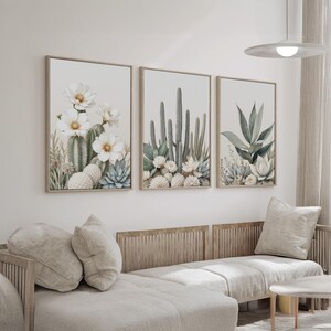 May include: Three framed botanical prints featuring watercolor illustrations of cacti and succulents. The artwork showcases a neutral color palette with beige, green, and white tones. The prints are displayed above a light-colored sectional sofa.