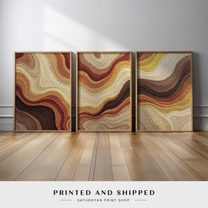 May include: Three framed abstract art prints with a warm color palette of browns, tans, and yellows. The prints feature a layered, wavy design. The text "PRINTED AND SHIPPED" is at the bottom.