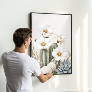 May include: A framed art print featuring a watercolor illustration of a cactus with large white flowers and a light background. The artwork includes green cacti, white flowers with yellow centers, and blue-green succulents.