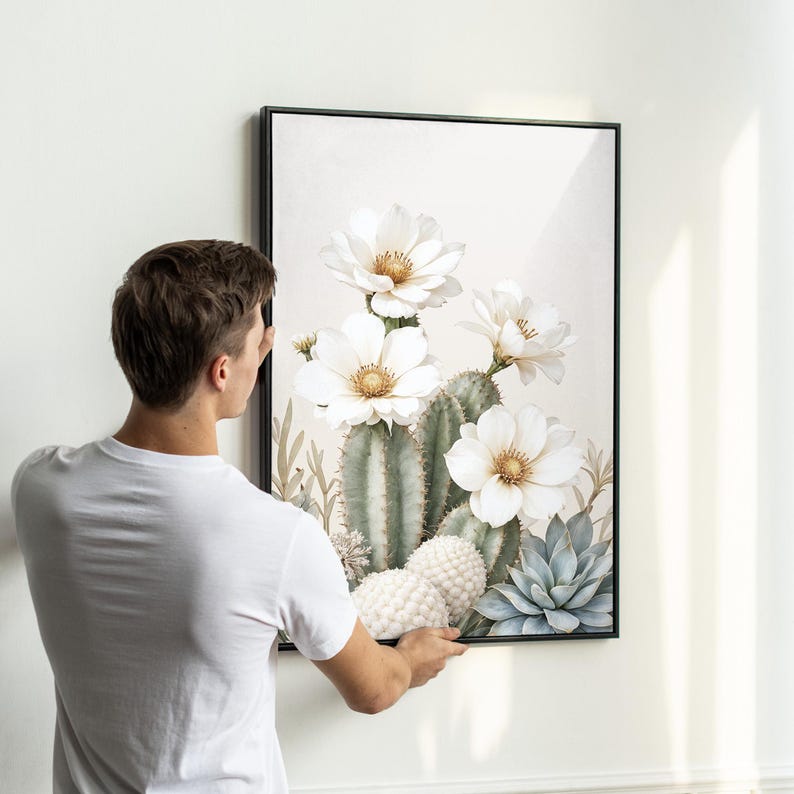 May include: A framed art print featuring a watercolor illustration of a cactus with large white flowers and a light background. The artwork includes green cacti, white flowers with yellow centers, and blue-green succulents.