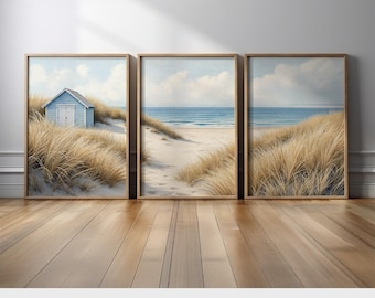 May include: Three framed prints depicting a serene beach scene. The artwork features a blue beach hut, sand dunes, and the ocean under a cloudy sky. The prints are in wooden frames and rest on a wooden floor. The text "PRINTED AND SHIPPED" is at the bottom.