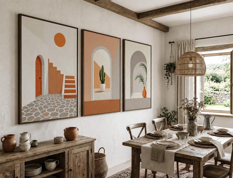 May include: A triptych of framed wall art prints featuring architectural scenes with arched doorways, a staircase, a cactus, and a potted plant in shades of orange, beige, and gray, displayed on a textured white wall above a wooden sideboard.