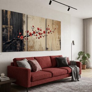 K&ouml;nnte beinhalten: Ein dreiteiliges Leinwand-Wandkunst-Set mit einem dunkel schwarzen und goldenen strukturierten Hintergrund auf der linken Seite, der in einen hellbeigen Hintergrund auf der rechten Seite &uuml;bergeht, mit einem Ast voller leuchtend roter Kirschbl&uuml;ten.
