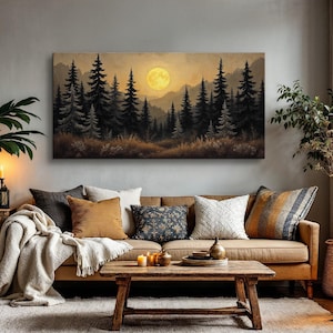 May include: A brown leather sofa with a throw blanket and pillows in front of a canvas print of a forest scene with a full moon. The print is framed and hanging on a gray wall.