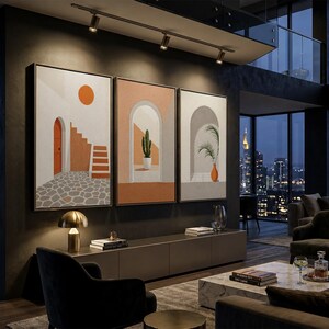 May include: A triptych of framed wall art prints featuring architectural scenes with arches, a cactus, a potted plant, and a sun, displayed on a dark wall above a long media console in a modern living room with floor-to-ceiling windows.