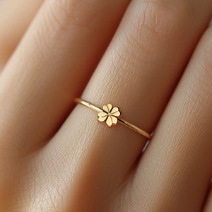 Puede incluir: Un delicado anillo de oro con un diseño de trébol de cuatro hojas. El anillo es fino y minimalista, con el trébol centrado en la banda. El anillo se muestra en un dedo, destacando su simple elegancia. Una joya para el uso diario.