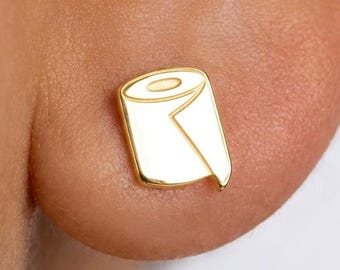 May include: A gold-toned stud earring shaped like a roll of toilet paper. The earring features a smooth, polished surface with engraved lines defining the top edge and the loose end of the paper roll, creating a distinct and recognizable silhouette.