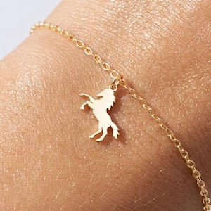 Puede incluir: Una delicada pulsera de cadena en tono dorado que presenta un pequeño dije plano con la silueta de un caballo en posición encabritada. La pulsera está construida con eslabones circulares finos y se asegura con un cierre sencillo.