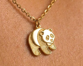 May include: A gold-toned necklace featuring a pendant shaped like a panda bear. The panda pendant has a textured finish on its body and smooth, polished edges. The pendant hangs from a delicate gold-toned chain with small, round, interlocking links.