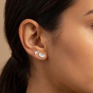 Sterling silver baseball stud earring worn beside a silver hot dog stud on one earlobe