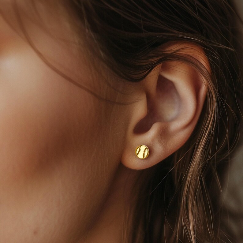 Gold baseball stud earring worn on the earlobe of a woman with brown hair