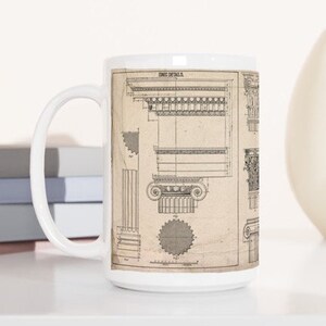 May include: A white ceramic mug featuring architectural blueprint details in sepia tones. The mug's design includes detailed drawings of columns, capitals, and other classical architectural elements. The text "IONIC DETAILS" is visible at the top of the mug.