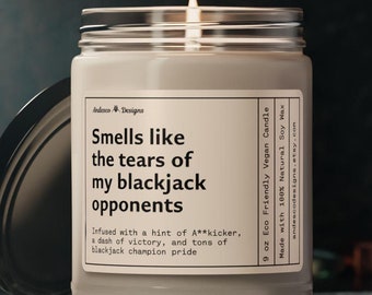 May include: A 9 ounce soy wax candle with a black and white label that reads "Smells like the tears of my blackjack opponents. Infused with a hint of A**kicker, a dash of victory, and tons of blackjack champion pride."