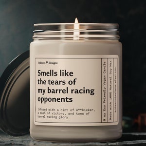 May include: A 9 ounce soy wax candle in a clear glass jar with a black lid. The candle is labeled "Smells like the tears of my barrel racing opponents" and "Infused with a hint of A**kicker, a dash of victory, and tons of barrel racing glory".