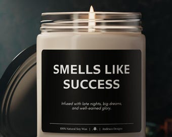 Könnte beinhalten: Eine beige Kerze in einem Glasgefäß mit einem schwarzen Etikett, auf dem "Smells Like Success" und "Infused with late nights, big dreams, and well-earned glory." steht. Das Etikett enthält auch den Text "100% Natural Soy Wax | Andesco Designs".
