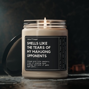 May include: A 9 ounce soy wax candle in a clear glass jar with a black label that reads "Smells Like The Tears Of My Mahjong Opponents". The label also includes the text "Infused with tile mastery, a dash of winning hand strategy and lots of game right glory."