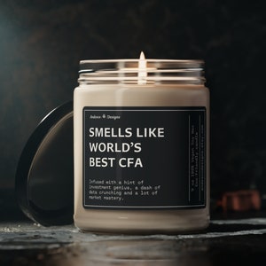 May include: A beige candle with a black label that reads "Smells Like World's Best CFA" and "Infused with a hint of investment genius, a dash of data crunching and a lot of market mastery." The candle is lit and the flame is visible.