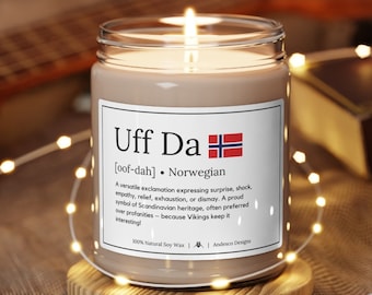 May include: A brown candle with a white label that reads "Uff Da [oof-dah] Norwegian" and a small Norwegian flag. The label explains that "Uff Da" is a versatile exclamation expressing surprise, shock, empathy, relief, exhaustion, or dismay. It is a proud symbol of Scandinavian heritage, often preferred over profanities because Vikings keep it interesting! The candle is on a wooden coaster and surrounded by white fairy lights.