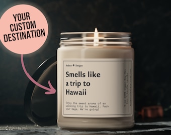 May include: A beige candle with a white label that reads "Smells like a trip to Hawaii" and "Enjoy the sweet aroma of an upcoming trip to Hawaii. Pack your bags, We're going!" The candle is in a clear glass jar with a black lid. The candle is lit and the flame is visible.