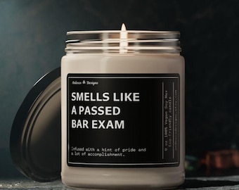 May include: A white candle in a glass jar with a black label that reads "Smells Like A Passed Bar Exam". The label also says "Infused with a hint of pride and a lot of accomplishment."