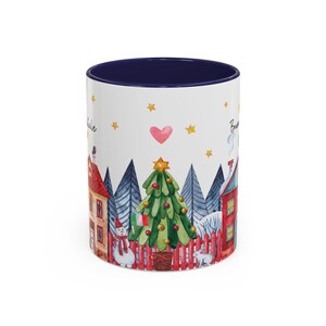 May include: White ceramic mug with a blue rim, featuring a watercolor illustration of a winter scene with a Christmas tree, two houses, a snowman, and two rabbits. The text "Believe" and "Believe" is visible on the mug.