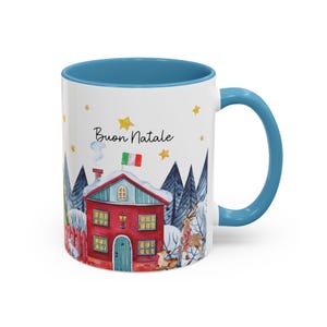 May include: White ceramic mug with a blue interior and handle. The mug features a watercolor illustration of a red house with a green roof and white trim, surrounded by trees and snow. The Italian flag is on top of the house. The text "Buon Natale" is printed on the mug.