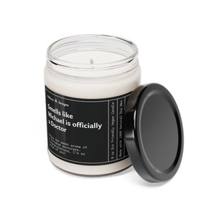 K&ouml;nnte beinhalten: Eine 9 Unzen Sojawachskerze in einem durchsichtigen Glasgef&auml;&szlig; mit schwarzem Deckel. Das Etikett lautet "Smells like Michael is officially a Doctor" und "Eco Friendly Vegan Candle".