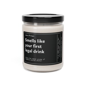 May include: A 9 ounce soy wax candle in a clear glass jar with a black lid. The candle is labeled "Smells like your first legal drink" and "Enjoy the sweet aroma of legally poured shots!" The label also states that the candle is 100% vegan soy wax and eco-friendly.