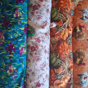 May include: Four vertical rolls of fabric featuring distinct patterns: a blue background with green seaweed and purple fish, a cream background with red floral prints, a brown background with pumpkins and orange slices, and an orange background with turkeys.