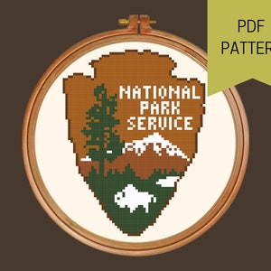 May include: Cross-stitch pattern for the National Park Service logo. The logo is a brown arrowhead with a mountain range, a pine tree, and a bison. The text "NATIONAL PARK SERVICE" is in white letters.