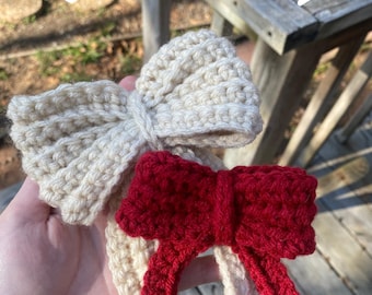 May include: Two handmade crochet bows, one cream-colored and one red, are displayed. The bows are held in a hand against a wooden background. The text "CROCHET BOW PATTERN" and "SCOOBYSCRAFTS" are visible.