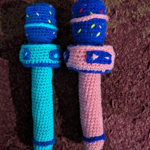 May include: Two handmade crochet microphones. One is turquoise with a blue top and the other is pink with a blue top. Both have a blue band around the base and a blue band around the top. The tops are decorated with colorful yarn.