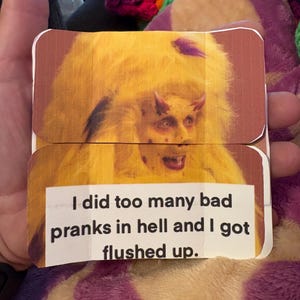 Pode incluir: Um cartão dobrado com uma imagem humorística de uma figura diabólica com chifres e uma juba amarela semelhante a pele. O cartão tem o texto: "I did too many bad pranks in hell and I got flushed up."