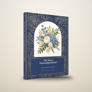 May include: A hardbound journal with a deep blue cover featuring gold botanical illustrations. The center displays a white arch containing a floral arrangement of white ranunculus, blue hydrangeas, and green leaves. Text reads: The Stress Processing Journal.