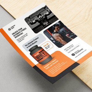 May include: A flyer advertising whey protein powder for building muscle. The flyer features a photo of a man lifting weights and a photo of a container of whey protein powder. The text on the flyer reads "Unlock Your Ultimate Fitness Potential!" and "The Ultimate Product to Build Muscles".