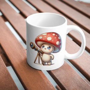 Peut inclure: Une tasse en c&eacute;ramique blanche avec une illustration de dessin anim&eacute; d'un personnage de champignon tenant un t&eacute;lescope. Le champignon est rouge avec des points blancs et a un visage mignon.